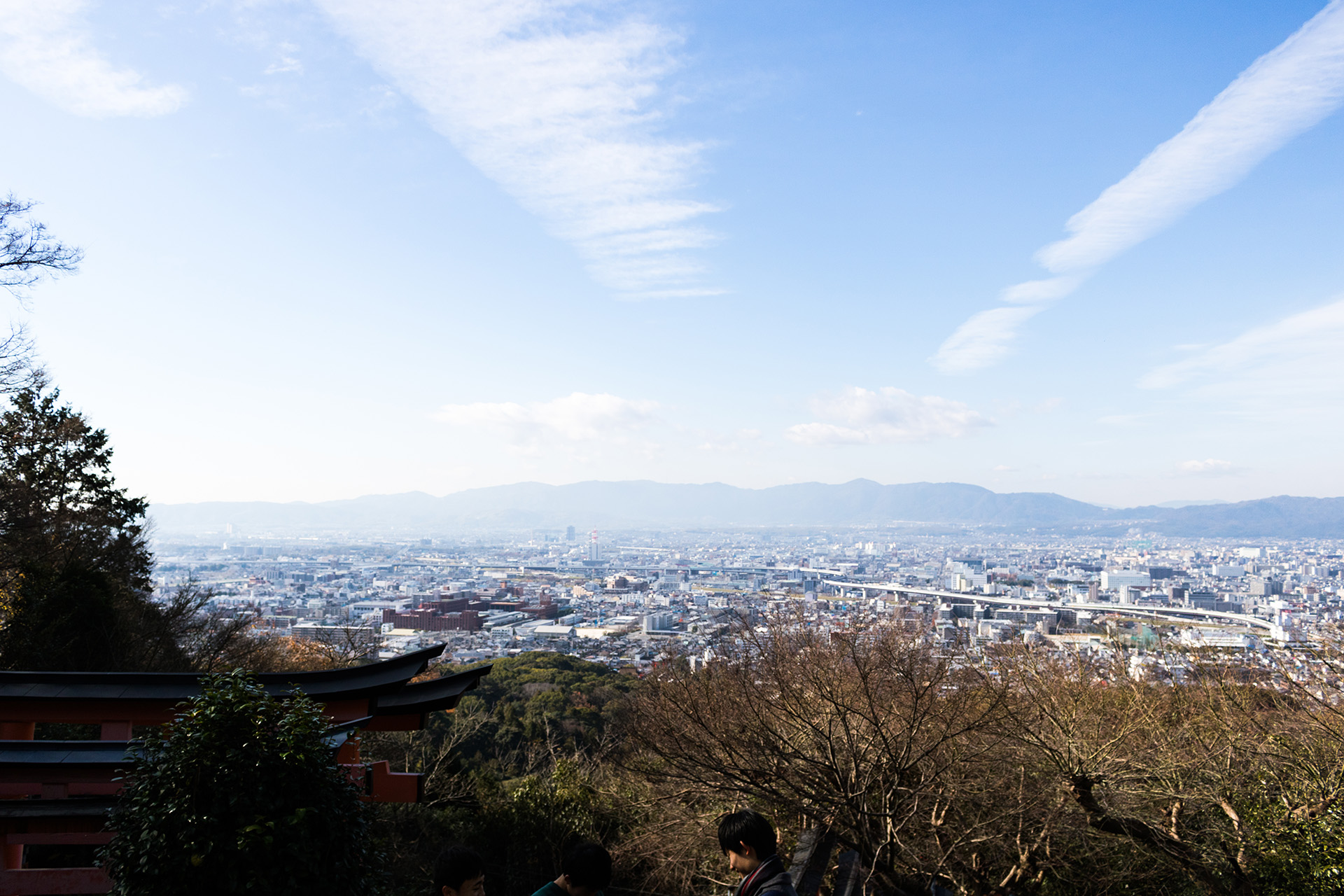 Dense city of short pale buildings seen from the top of a mountain, with another mountain in the distance, behind it the blue sky.